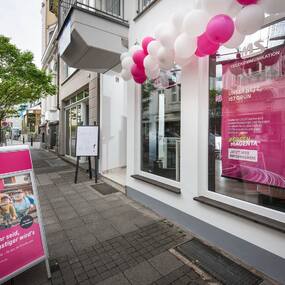 Telekommunikationsladen mit Telekom-Werbung, Schaufensterplakat und Luftballons am Eingang.